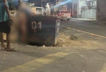 Homem observa corpo jogado em container de lixo