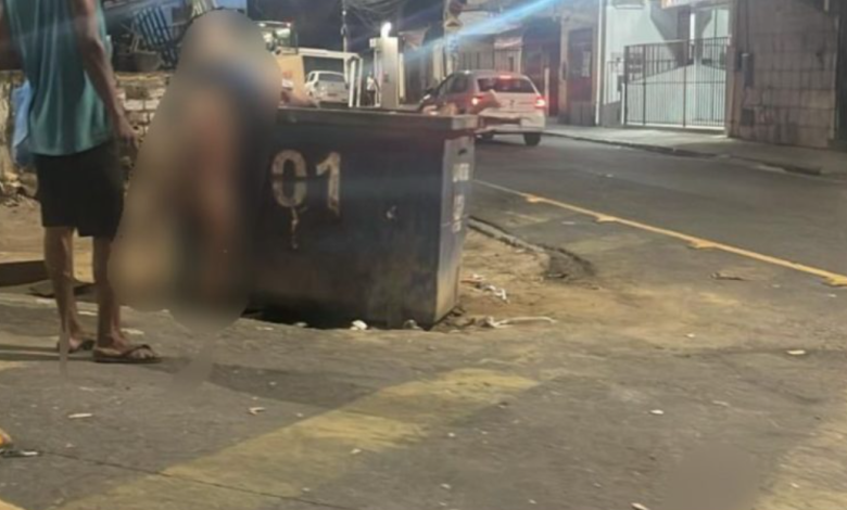 Homem observa corpo jogado em container de lixo